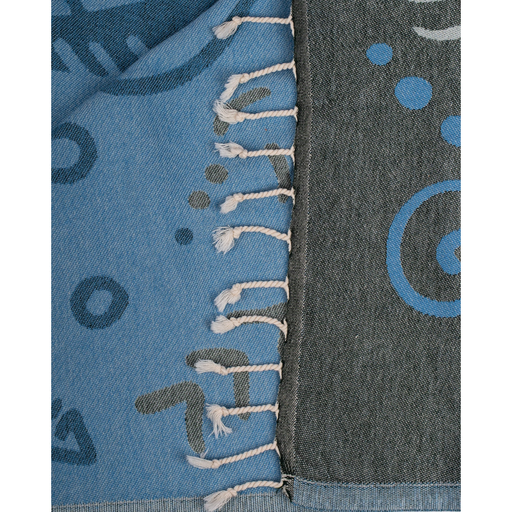 Close-up photo of a blue & gray beach towel with a shark design with blue abstract patterns and a white tassel edge on a white background.