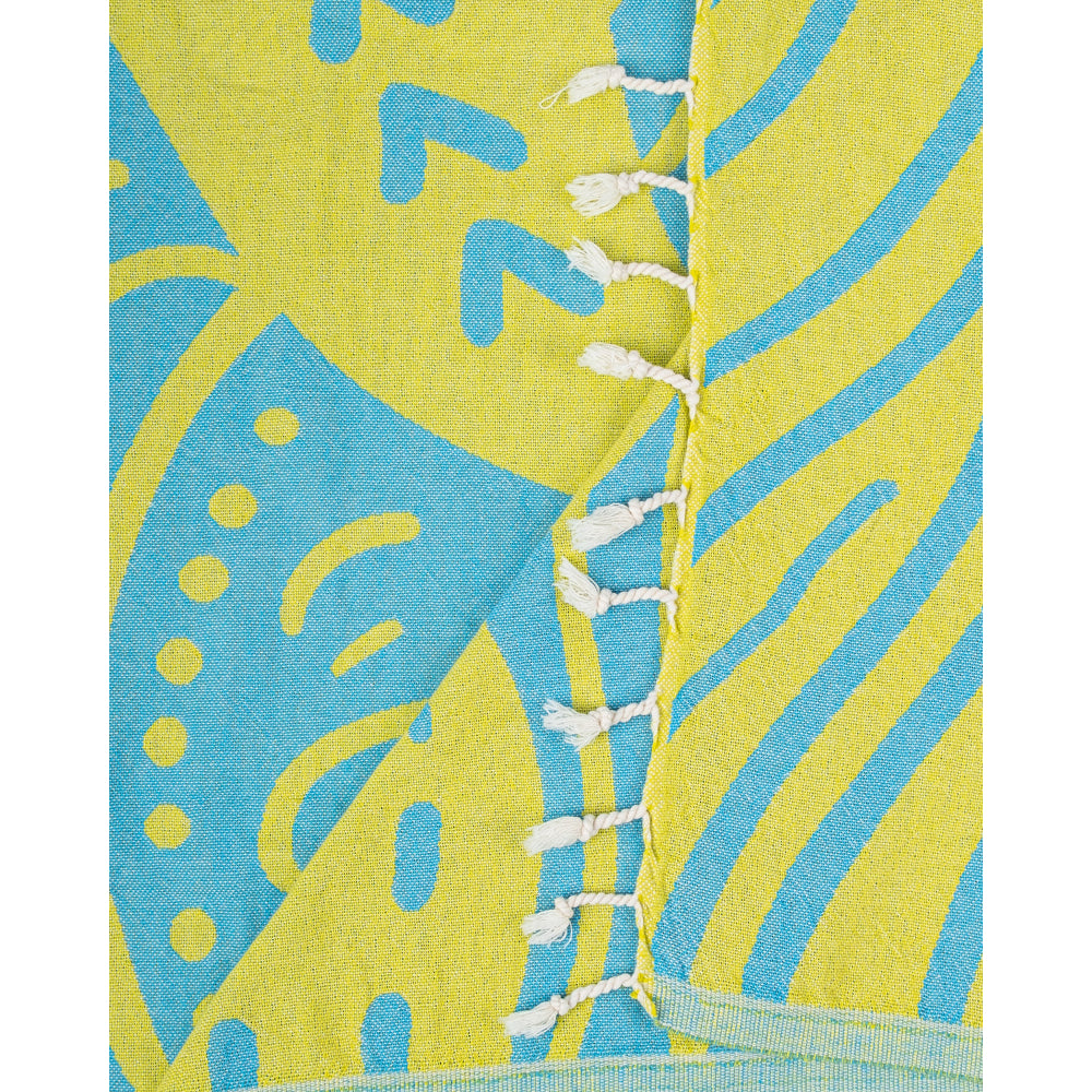 A close up of a beach towel with a blue and yellow shark design with a white tassel edge on a white background.
