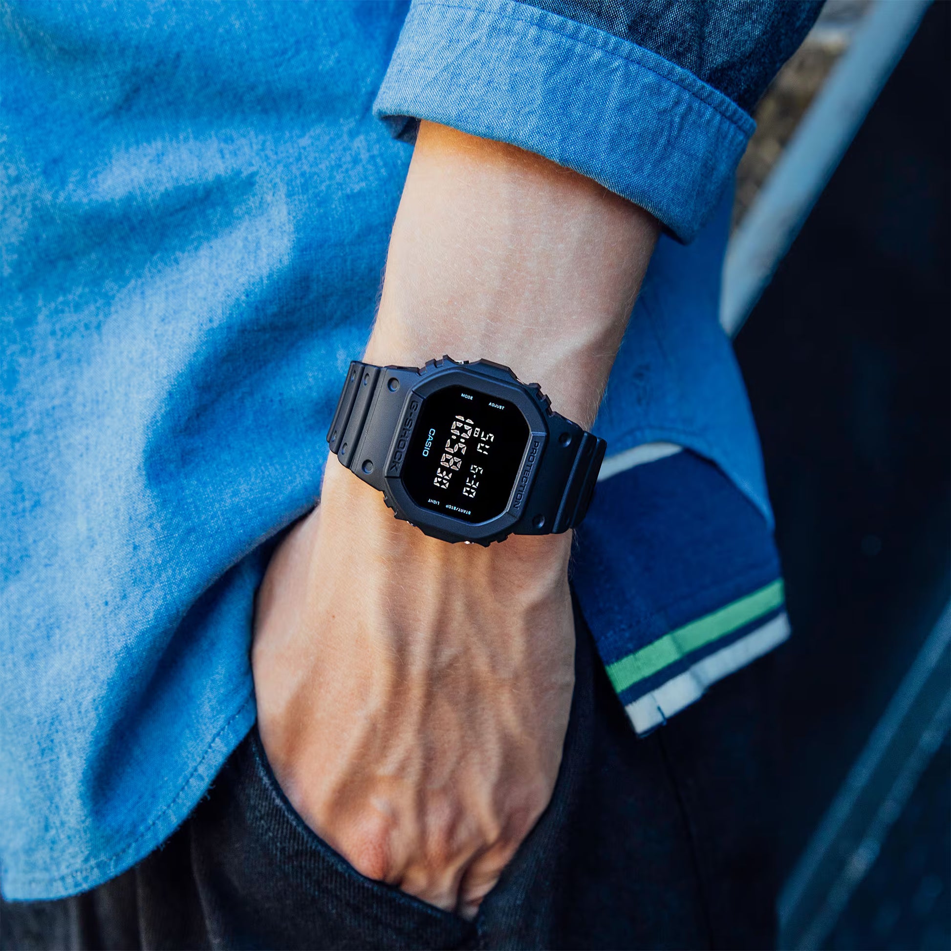 man's arm with black watch on with blue shirt and blue pants natural background