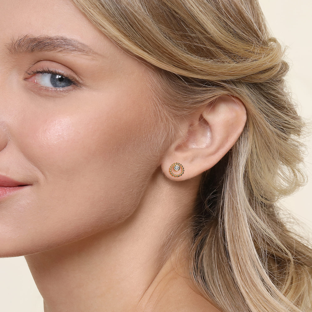 Close-up of a woman wearing gold hoop earrings with a neutral background