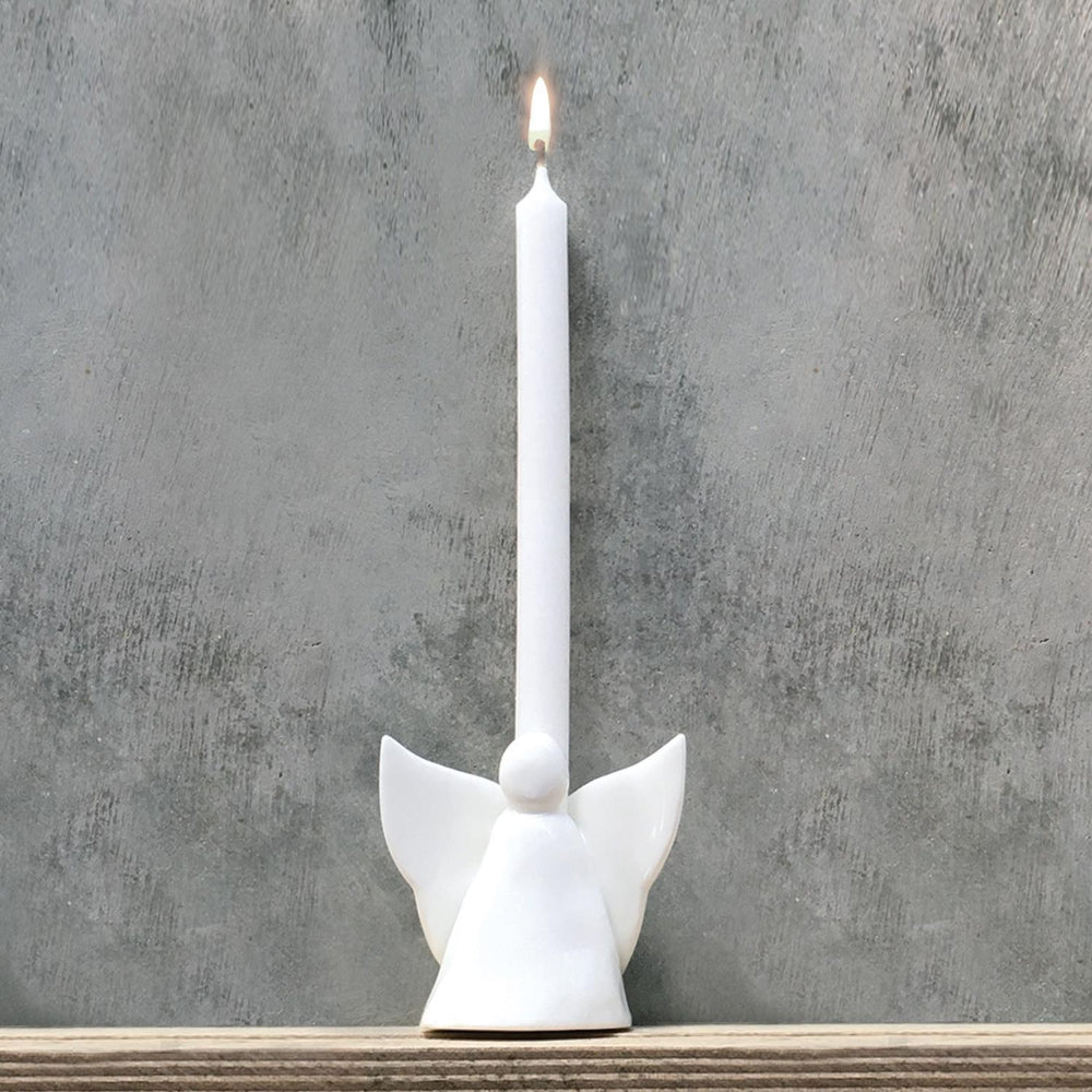 White ceramic decorative angel that can be used as a vase or candle holder with white candle on a wood shelf against a grey background.