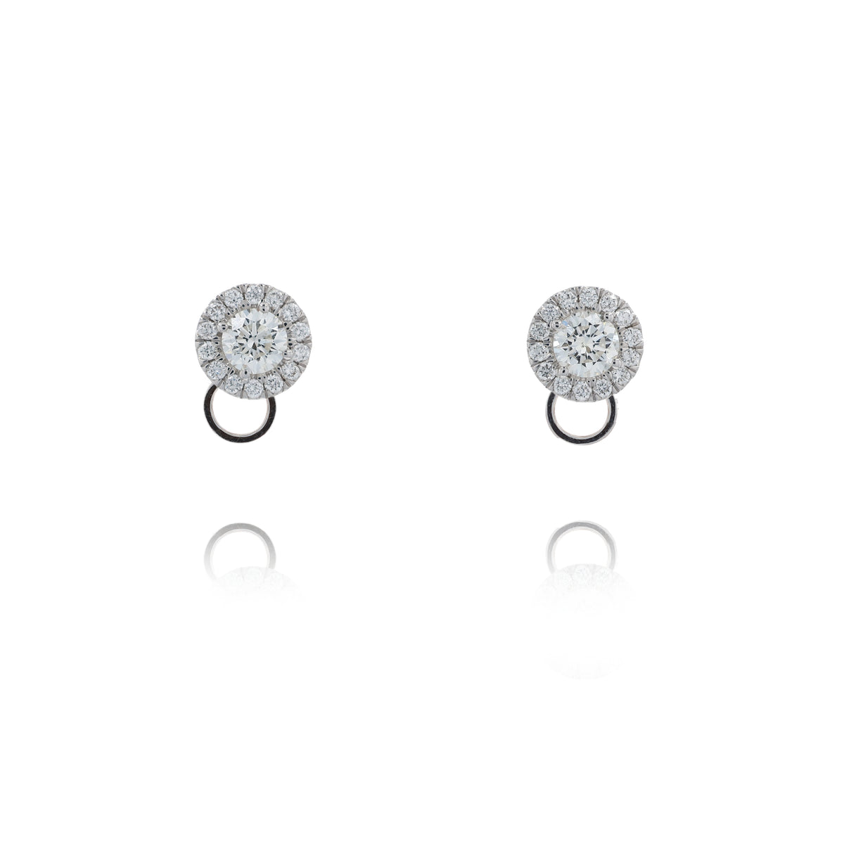 A pair of round halo stud earrings with clear gemstones in a silver-toned setting and a small circular drop below, shown on a white background with soft reflections.