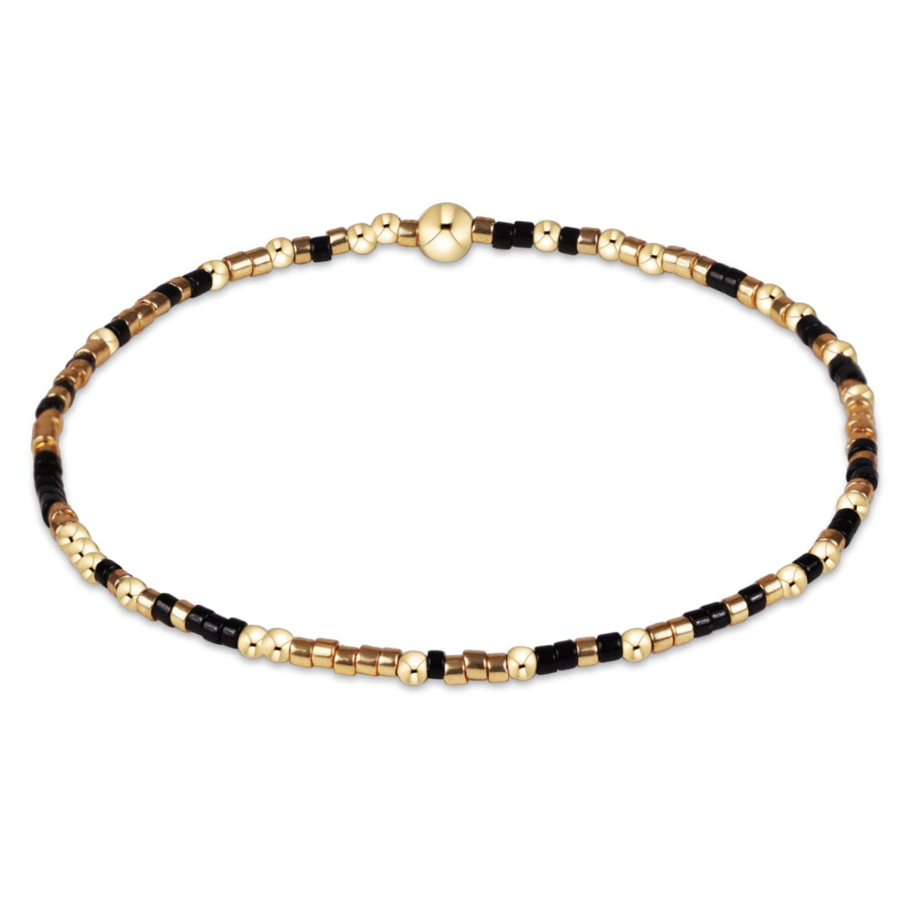 A delicate beaded bracelet with alternating black and gold metallic beads, featuring a small gold clasp, shown on a plain white background.