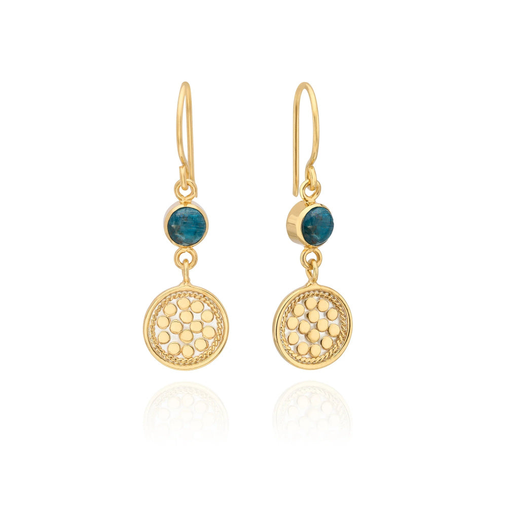 A pair of gold drop earrings with a small round dark blue gemstone and a larger round textured disc 