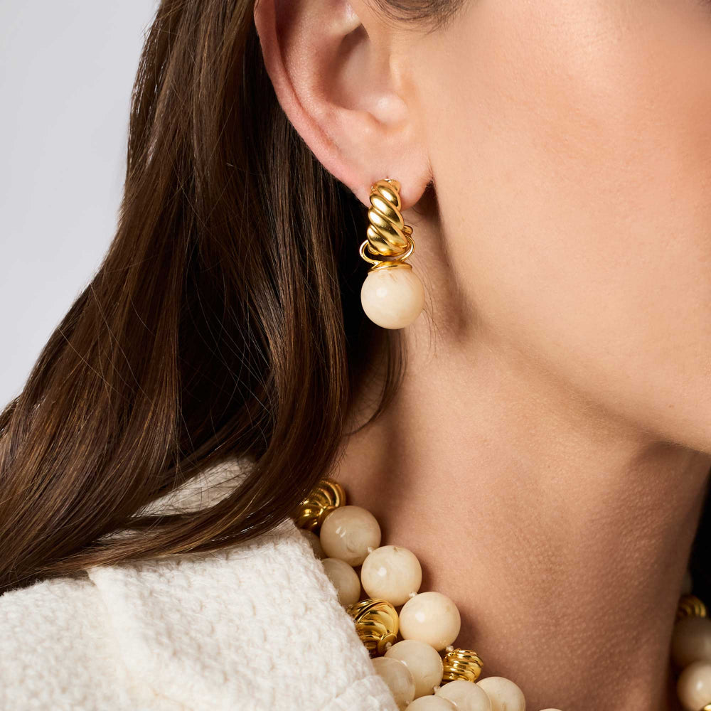 Close-up of a woman wearing a gold and cream pearl drop earring, with matching pearl and gold beads visible on her necklace.