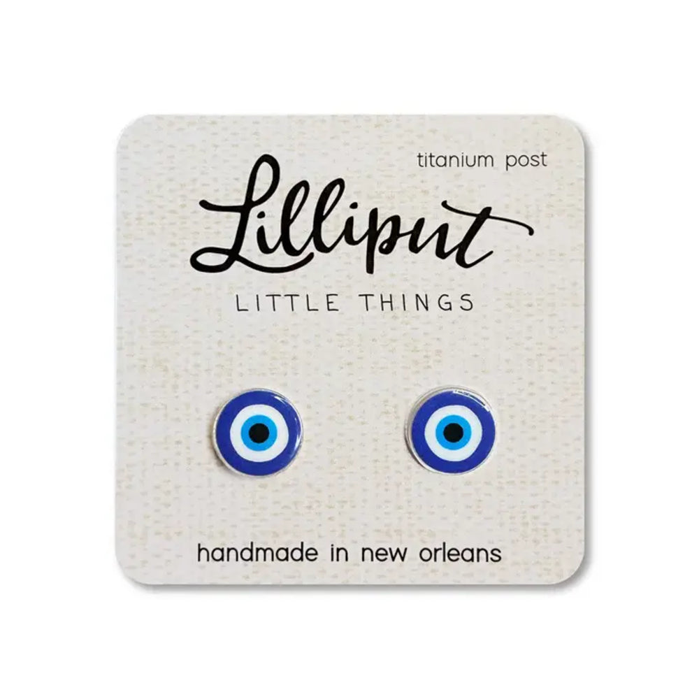 A pair of blue and white evil eye stud earrings mounted on a textured cream display card. The card features the brand name 'Lilliput LITTLE THINGS' and text indicating they are made of titanium post and handmade in New Orleans.