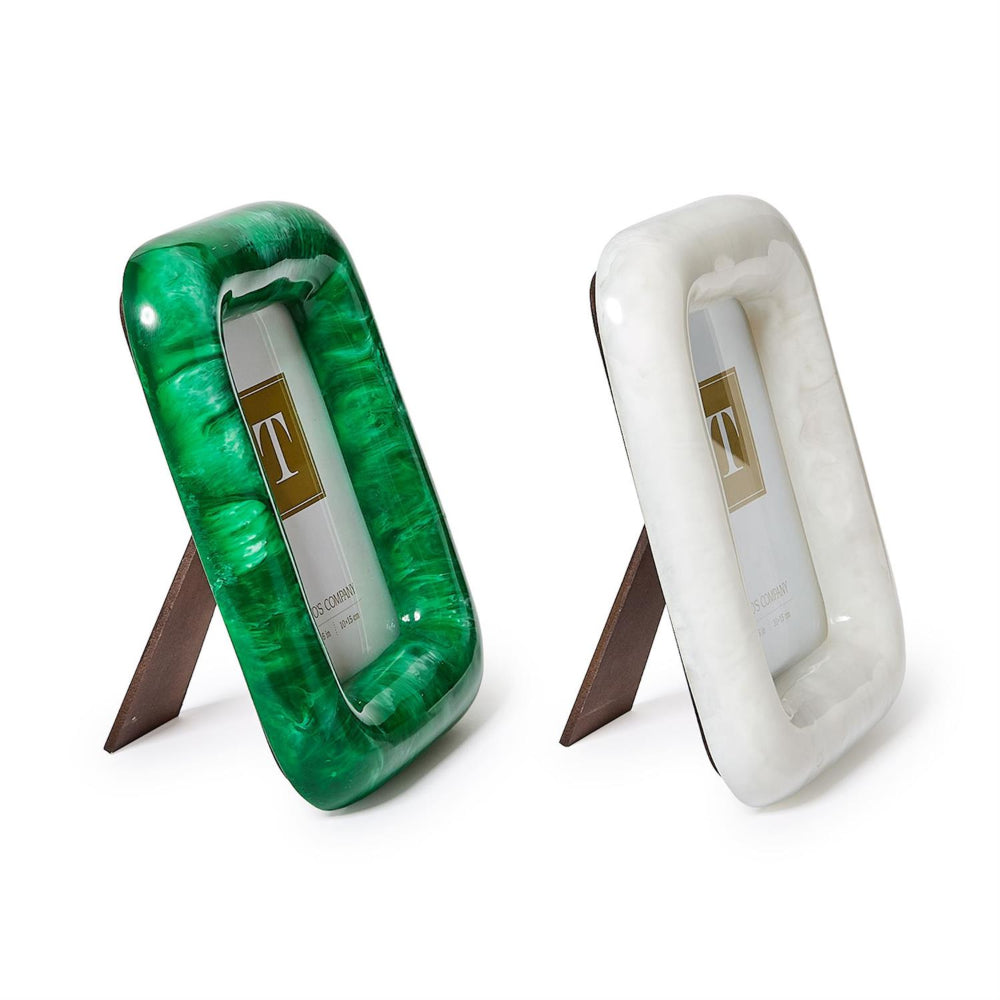 Two rectangular picture frames with arched legs on a white background, one in glossy green marbled resin and one in white marbled resin, both with a gold 'T' logo in the center.