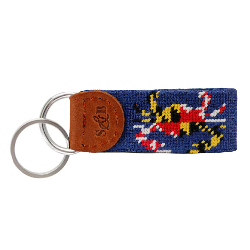 A needlepoint key fob featuring the Maryland flag with a crab design, on a blue background, with a leather loop and keyring.