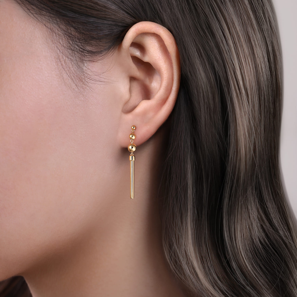 Gold earrings worn by a person with dark hair against a neutral background