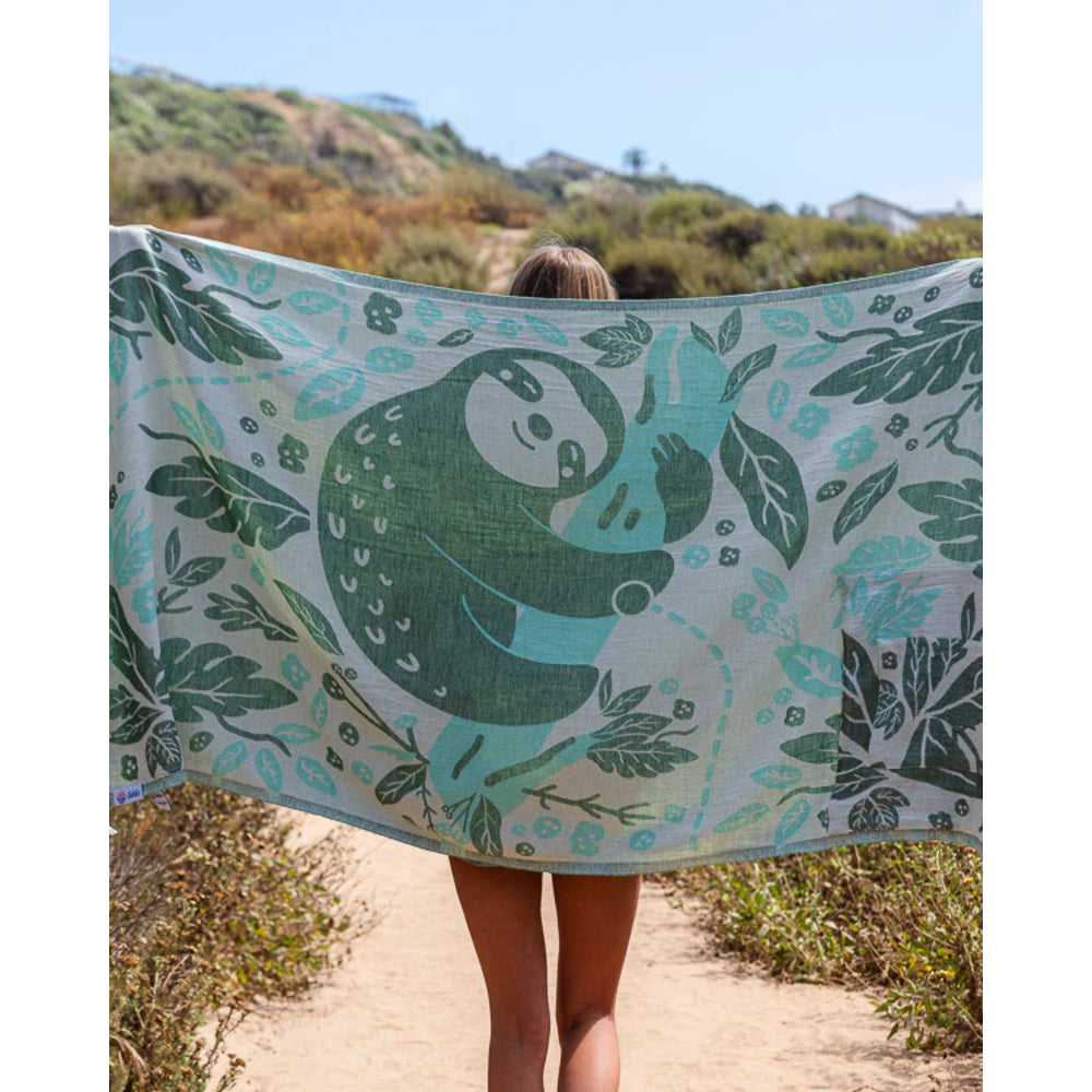 Person holding a large towel with a green and blue design outdoors.