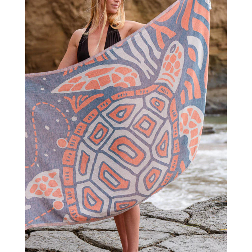 Person holding a large towel with a turtle design by a body of water.