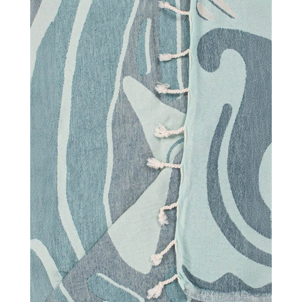 A close up photo of a blue Shark-themed beach towel with wave design and white tassel edge on a white background.