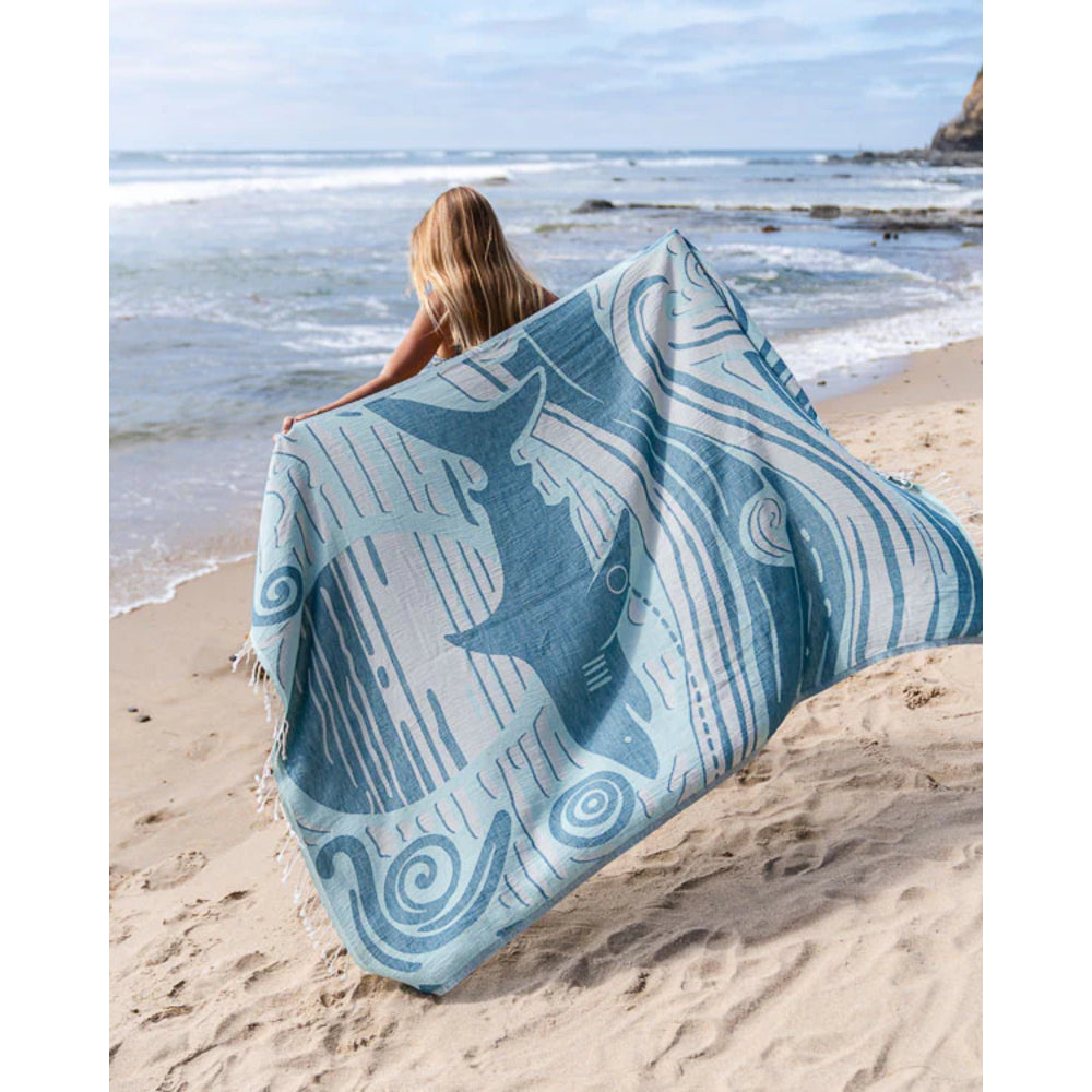 Person holding a blue and white patterned towel on a beach.