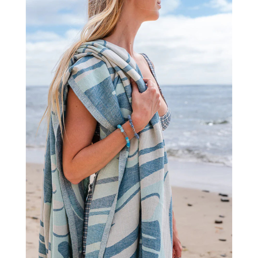 Woman holding a striped towel on a beach with ocean and sky in the background.