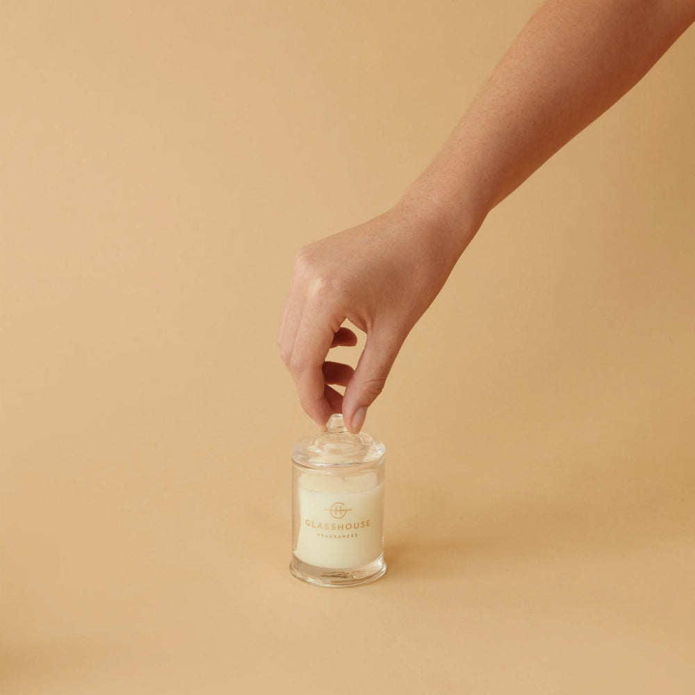 Hand reaching for a glass jar with a lid on a beige background