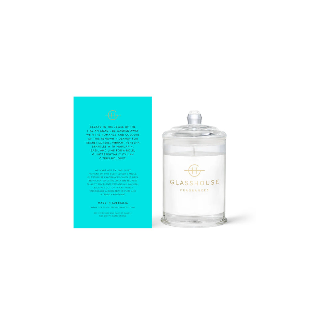 Back of a glasshouse candle and teal packaging with text next to a  clear " Passion In Positano" candle on a white background.