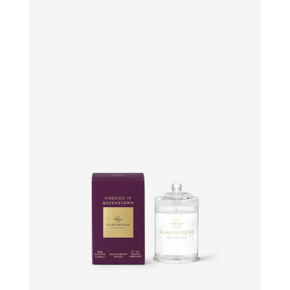 A clear glass jar candle with a clear lid and white wax sits beside its deep purple and gold retail box on a clean white background. The box reads 'Fireside in Queenstown' and 'Glasshouse Candle Co.