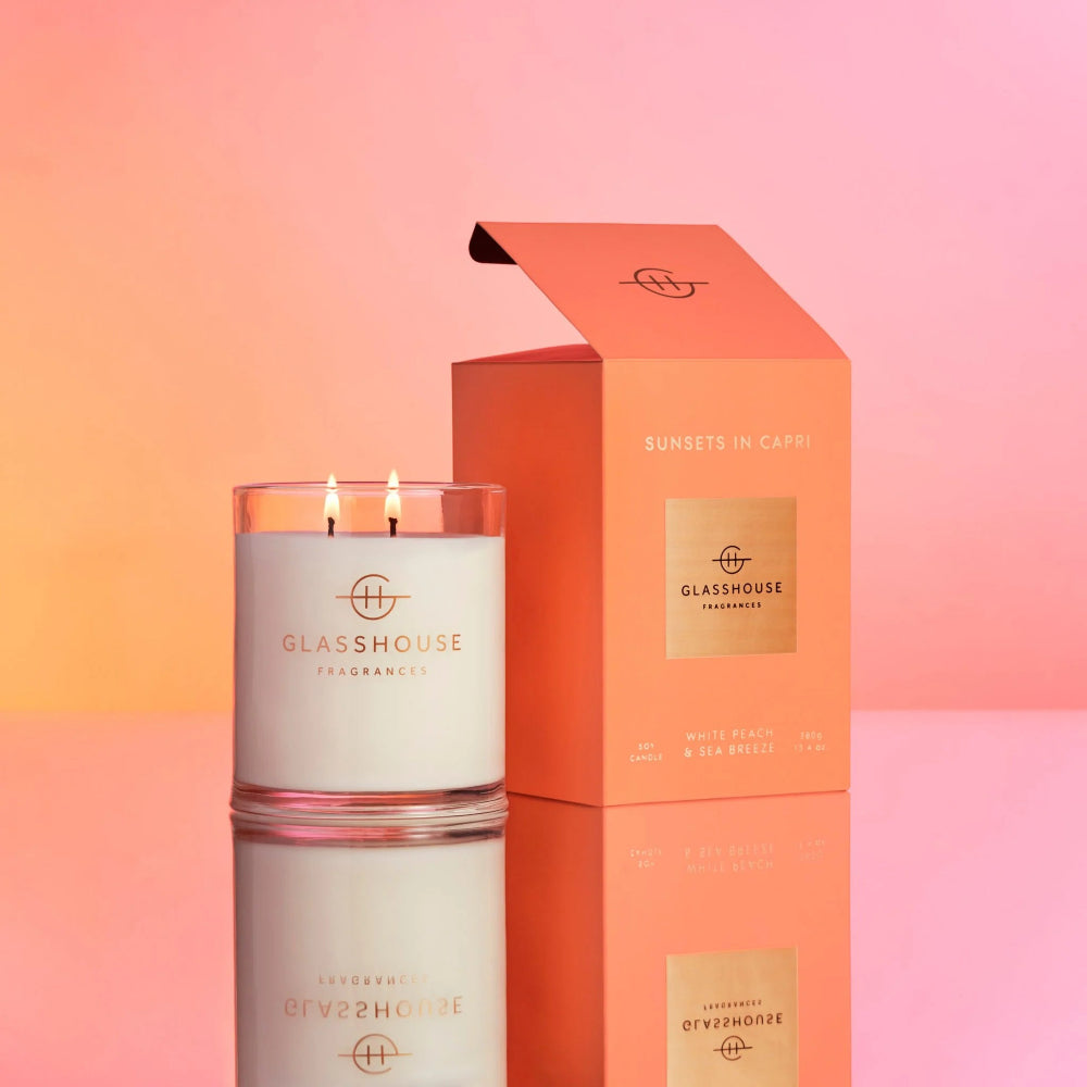 Glasshouse candle "Sunsets In Capri" and orange packaging on a gradient background.