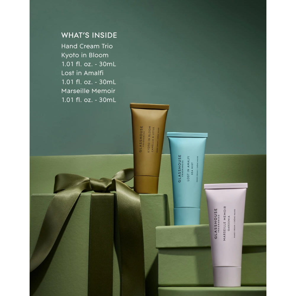 Three hand cream tubes in metallic gold, light blue, and pale lavender are displayed on green gift boxes with a green ribbon, against a muted green background. White text on the left lists the included scents: Kyoto in Bloom, Kyoto in Amalfi, and Marseille Memoir.