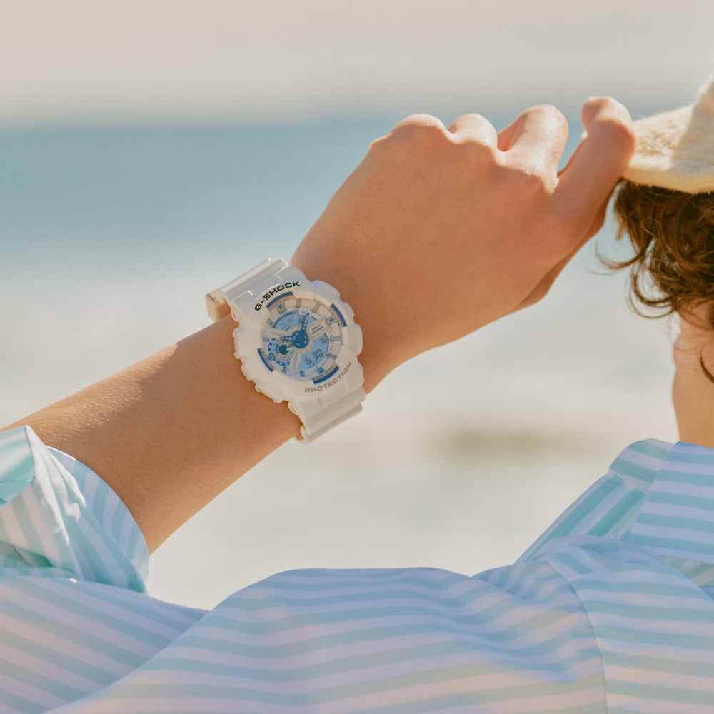 Person wearing a Casio watch with a blue floral design against a blurred beach background