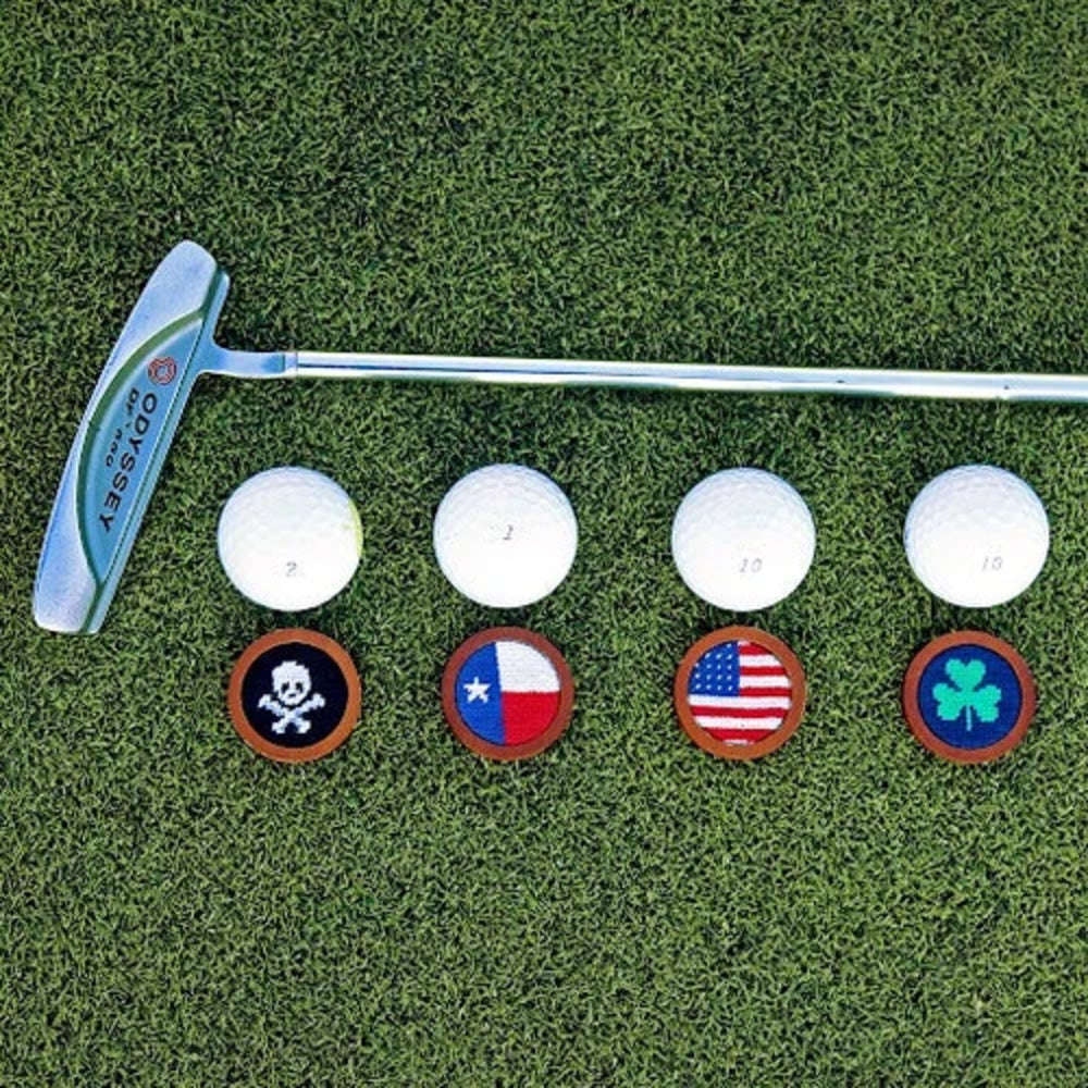 Golf putter with four golf balls and four different ball markers on a grass surface