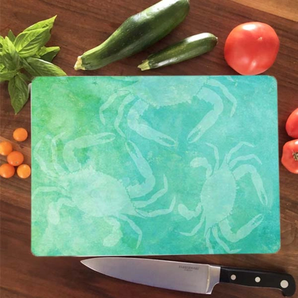 Green cutting board with crab design on a wooden surface with vegetables and a knife.