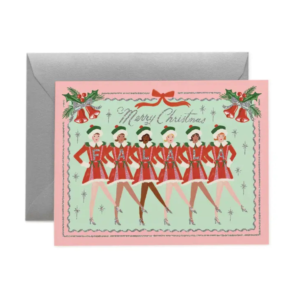 A square Christmas greeting card with a pink border and an illustrated row of women in red holiday uniforms dancing under a red bow, with the words 'Merry Christmas' across the top. The card is shown in front of a plain gray envelope on a white background.