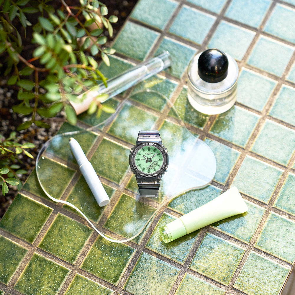 Green wristwatch on a tiled surface with a plant and other items.
