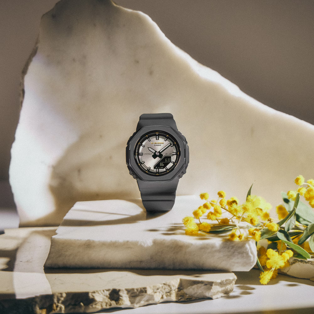Black watch on a stack of books with yellow flowers, all on a marble surface.