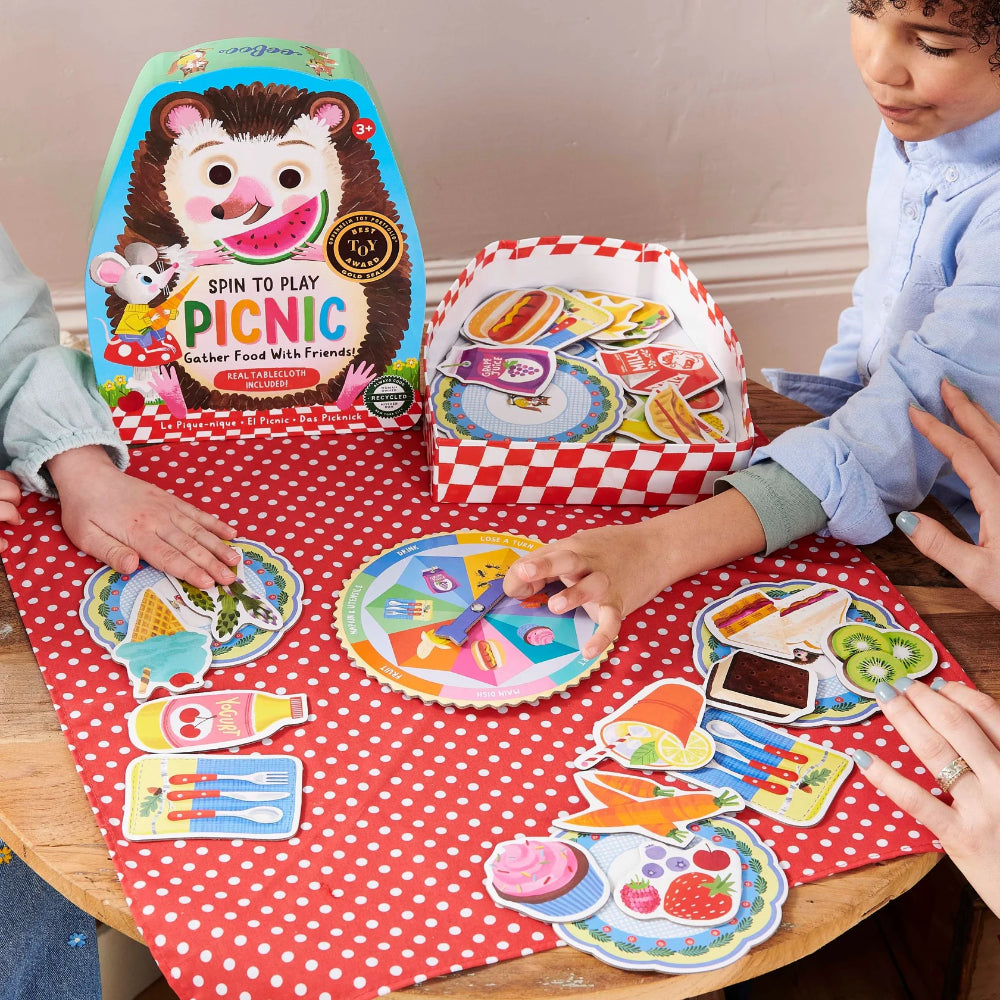 Children playing with a colorful picnic-themed game on a red polka dot tablecloth.