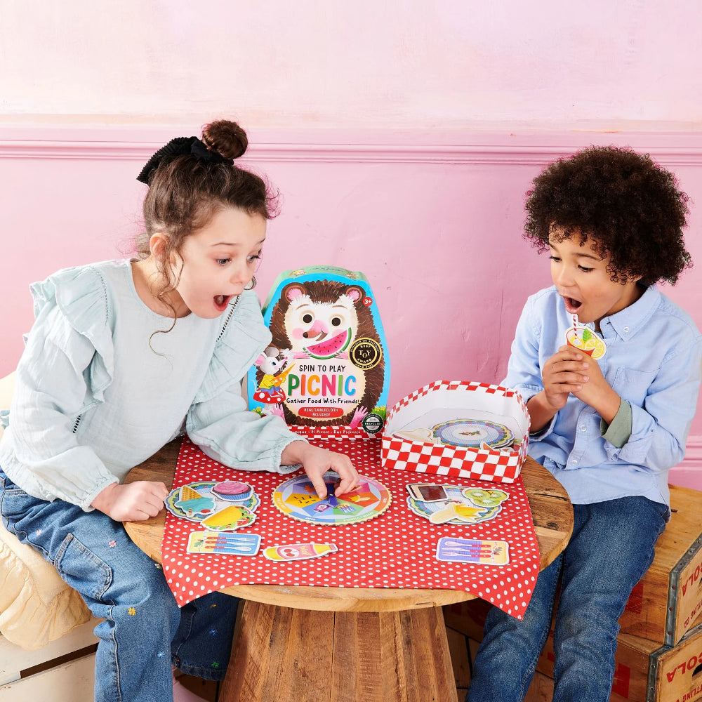 Two children playing with a picnic-themed toy set on a small table.