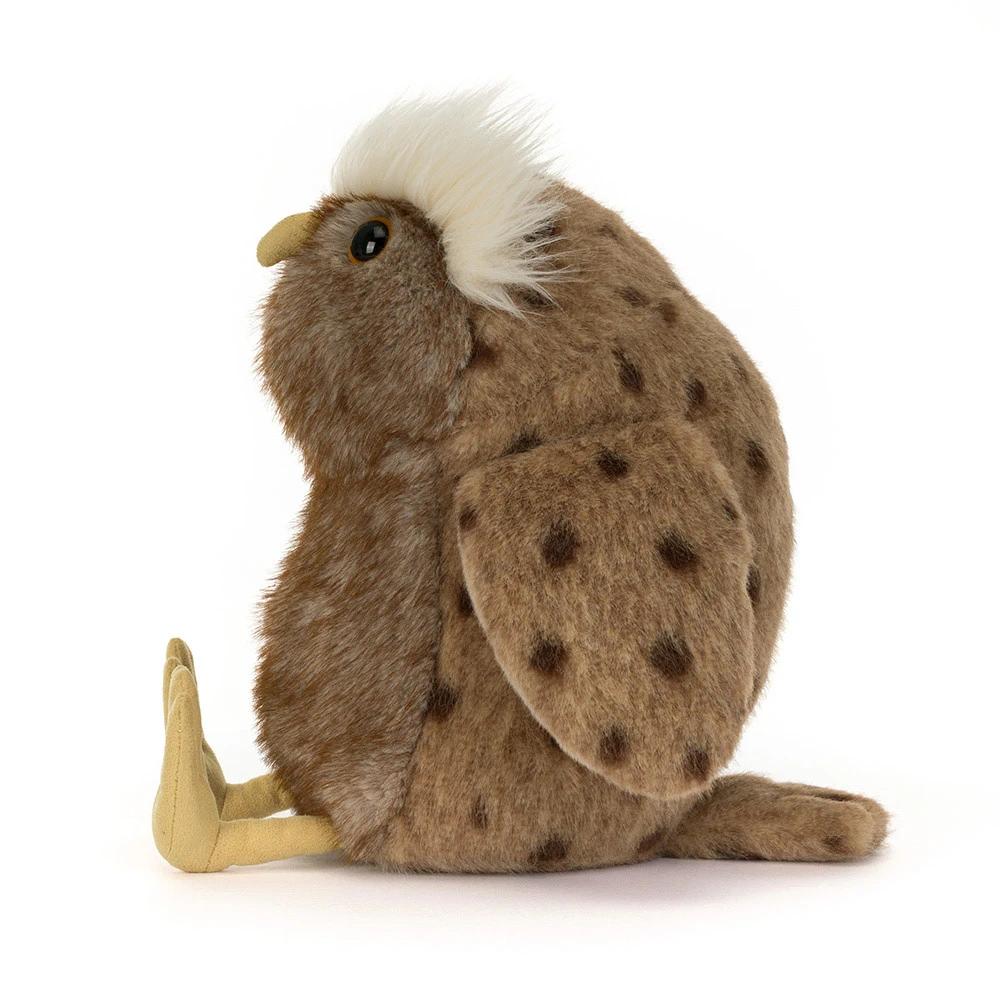 A plush stuffed animal shaped like a brown spotted owl, shown from the side on a clean white background. The bird has a fluffy white crest on its head, a yellow beak, tan legs, and dark brown spots across its brown fur.