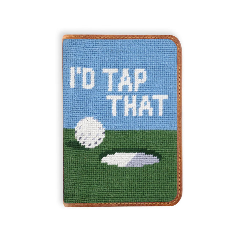 A rectangular leather scorecard holder with a golf theme, featuring a blue sky, green grass, a white golf ball, a hole, and the text 'I'D TAP THAT' in white. It has a brown leather border and is shown on a plain white background.
