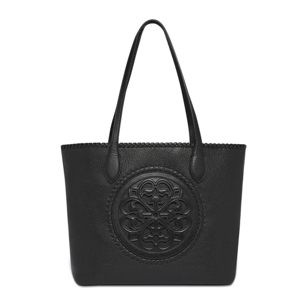 A black pebbled leather tote bag with dual top handles, a black leather tassel, and a large circular embossed floral monogram design on the front, set against a plain white background.