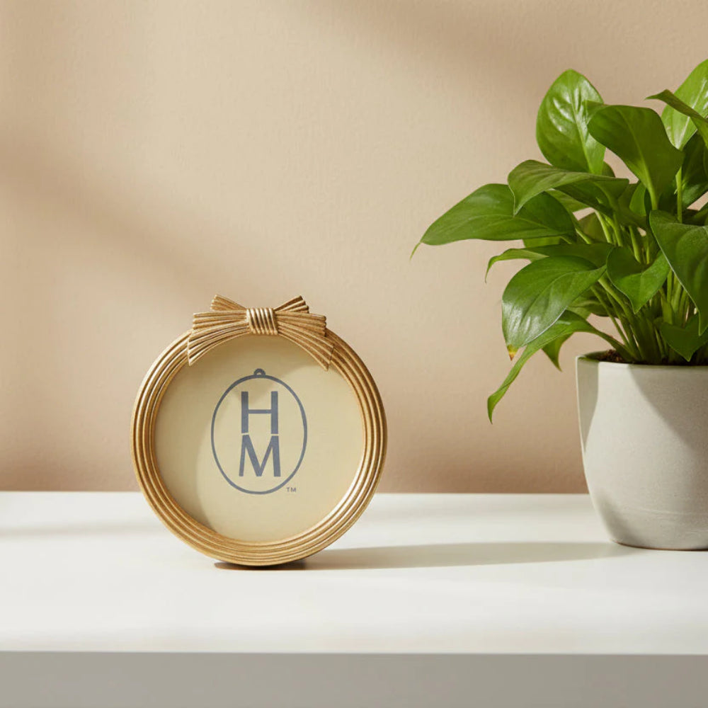 Gold decorative round frame with gold bow next to a potted plant on a beige surface.