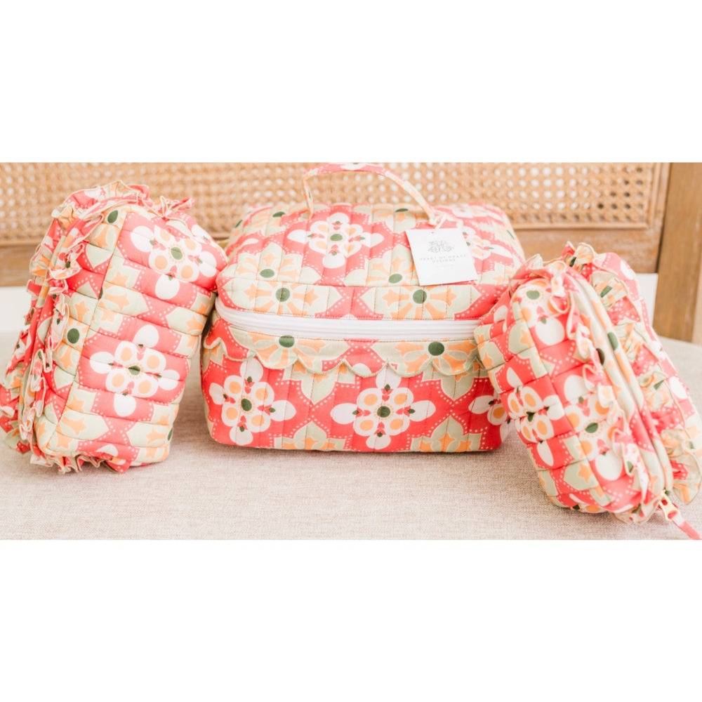 A set of three quilted fabric pouches with a coral pink and cream floral pattern, displayed on a neutral surface with a woven cane background.