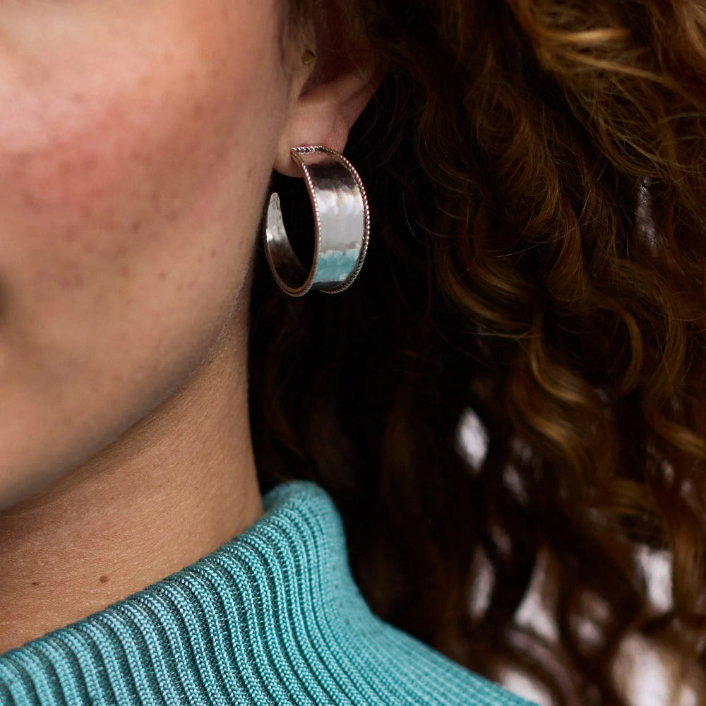 Close-up of a person wearing a silver hoop earring with a turquoise stone.