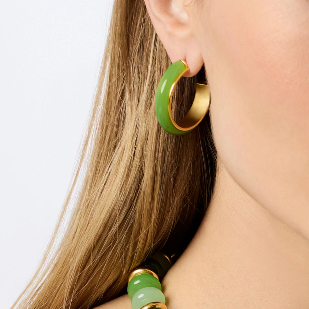 Close-up of a person wearing a green hoop earring with gold accents on a white background
