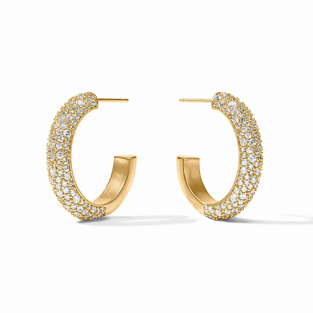 A pair of gold huggie hoop earrings paved with small clear stones, displayed on a clean white background.