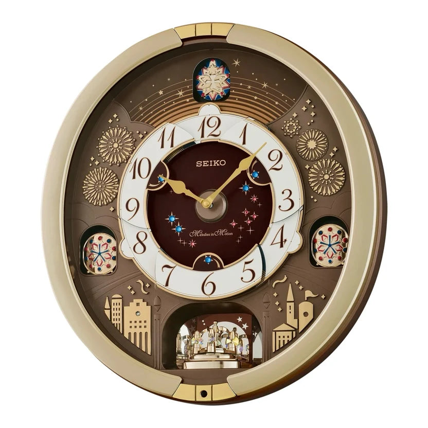 Seiko wall clock with a circular gold-toned frame and a dark brown and cream dial featuring decorative winter motifs, fireworks, stars, and cityscape details.