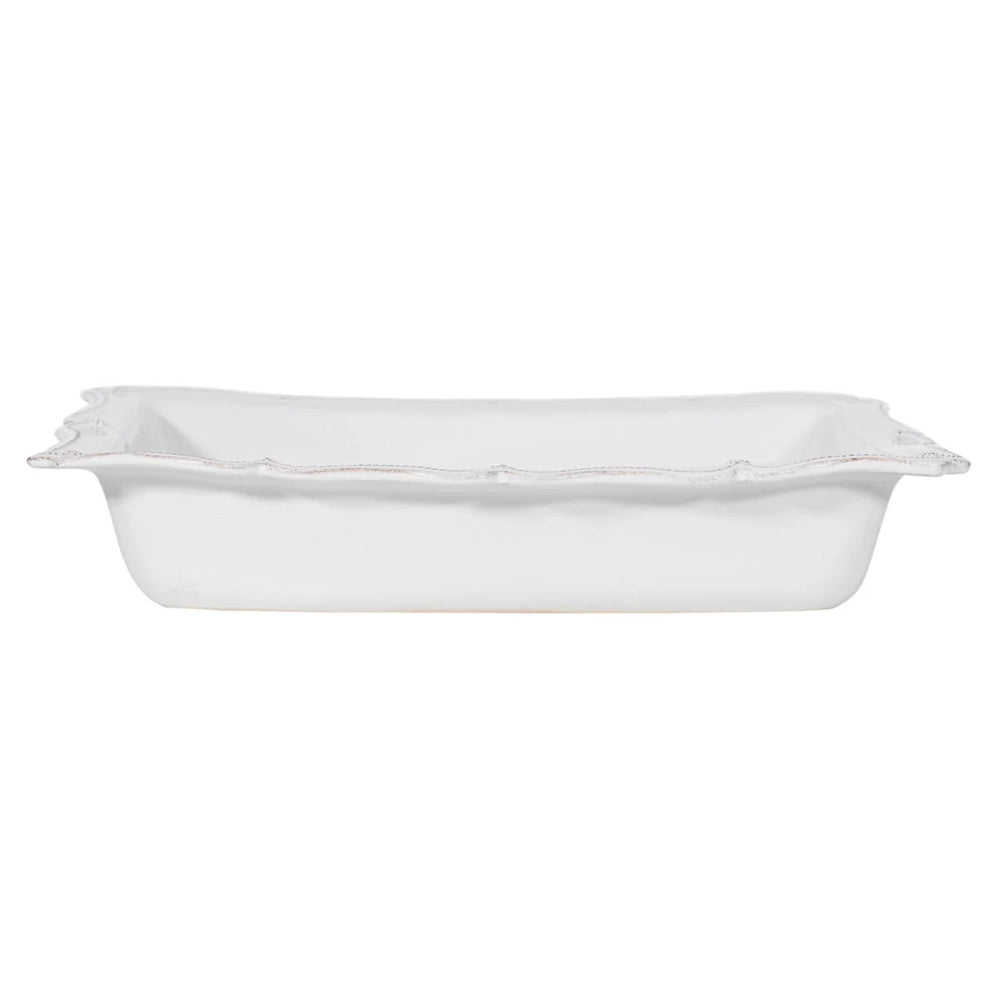 A white rectangular ceramic baking pan with a scalloped rim, shown from a side angle against a plain white background.