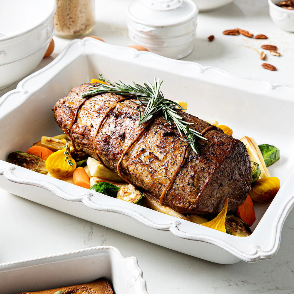 Roasted beef tenderloin with vegetables in a white dish on a marble surface