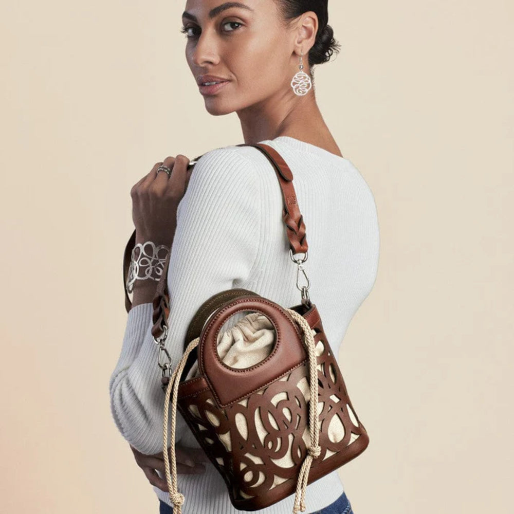 Woman carrying a brown handbag with intricate designs on a beige background