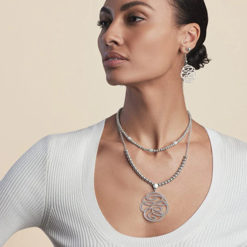 Woman wearing a silver necklace and earrings on a beige background