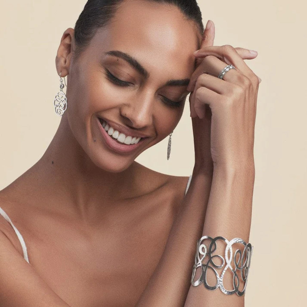 Woman wearing silver jewelry including earrings, a ring, and a bracelet on a beige background