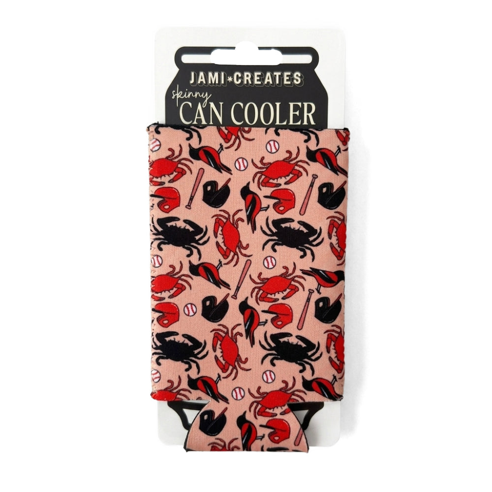 A Jami Creates Skinny Can Cooler featuring a red and black crab pattern on a light pink background, shown in its retail packaging against a white background.