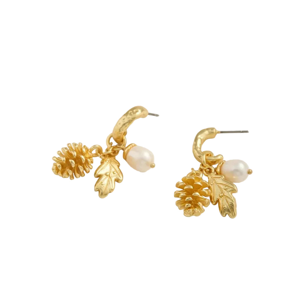 A pair of gold-toned drop earrings featuring pinecones, oak leaves, and small white pearl beads, displayed on a light cream background.