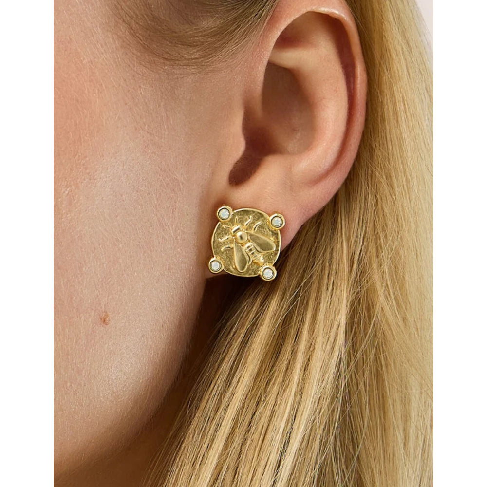 A close-up of a model's ear wearing a gold post earring with a raised insect motif and small white stone accents.