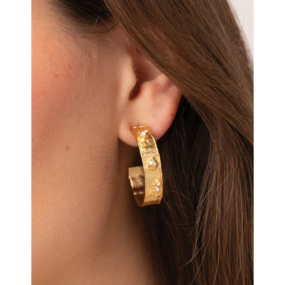 A close-up of a model's ear wearing a chunky gold huggie hoop earring adorned with small clear crystals.