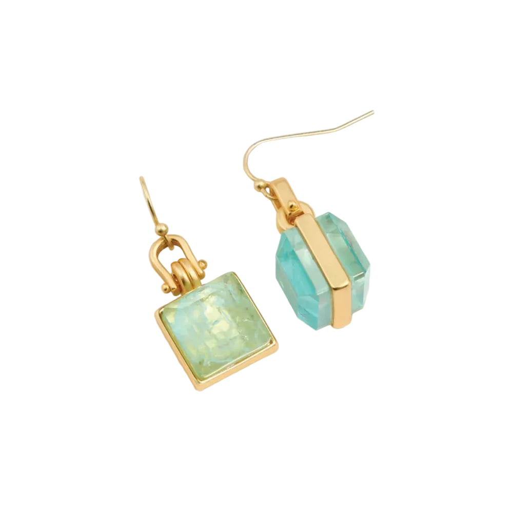 A pair of gold-tone drop earrings featuring faceted light blue-green stones, one square and one elongated hexagonal, set against a warm off-white background.